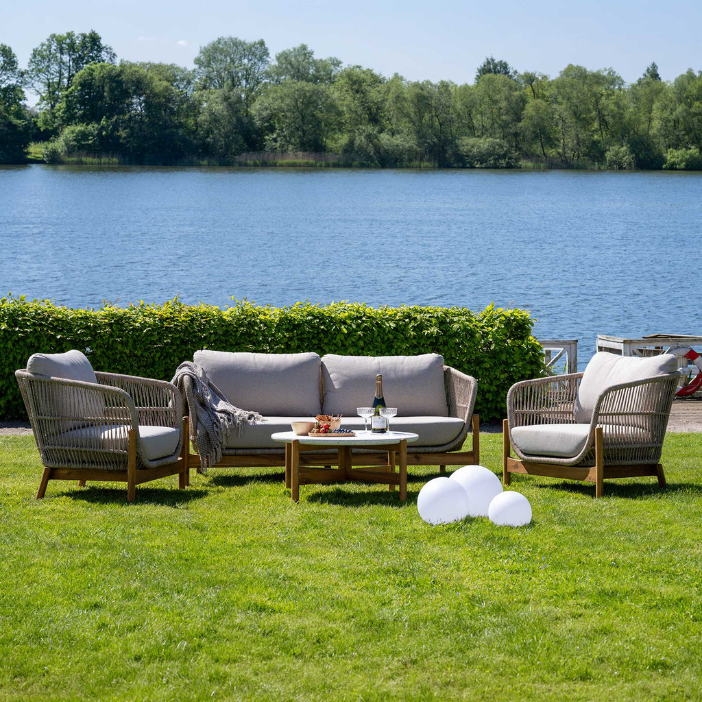 Outdoor furniture set on a grassy area by a lake with trees in the background