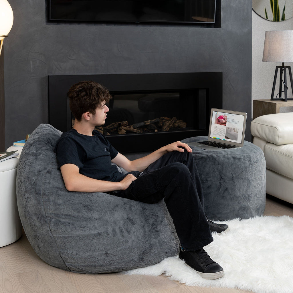 Person sitting on a bean bag in a living room with a fireplace and laptop.