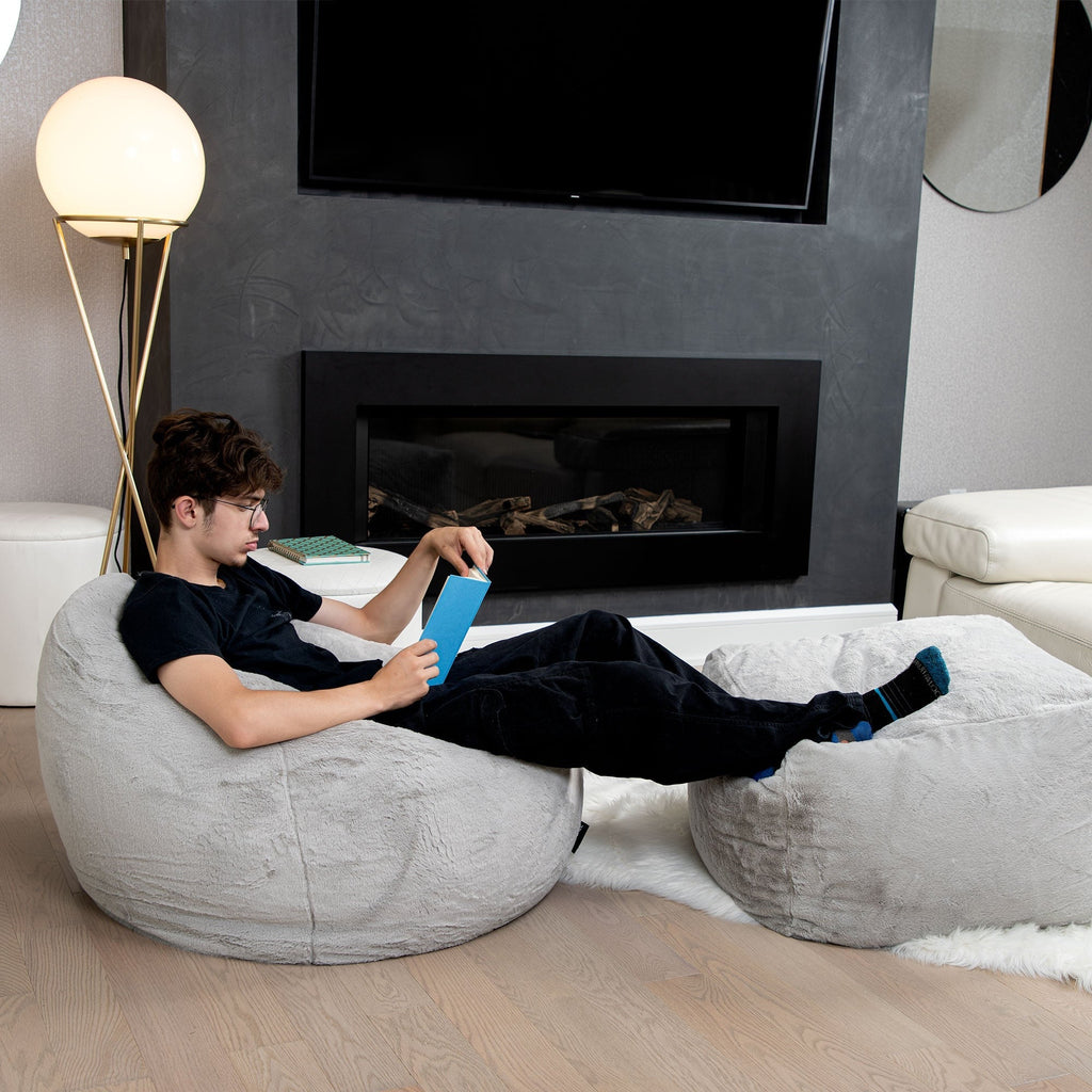 Person sitting on a bean bag chair in a modern living room with a fireplace and TV.