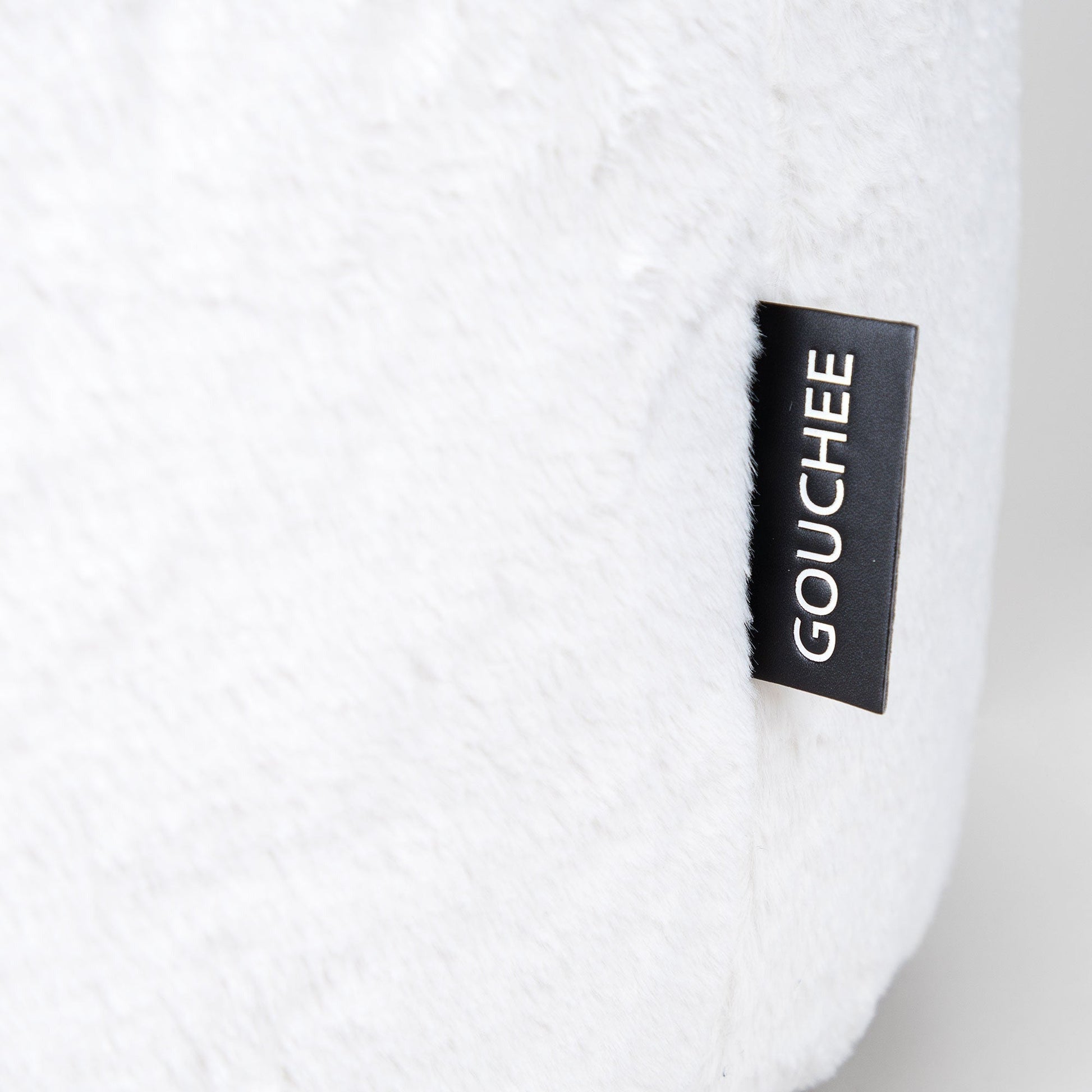 Close-up of a white product with a black label featuring the brand 'Gouchee' on a light gray background.