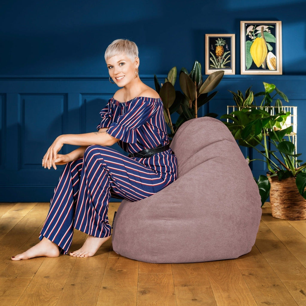 Woman in a striped outfit sitting on a bean bag chair against a blue wall with plants.