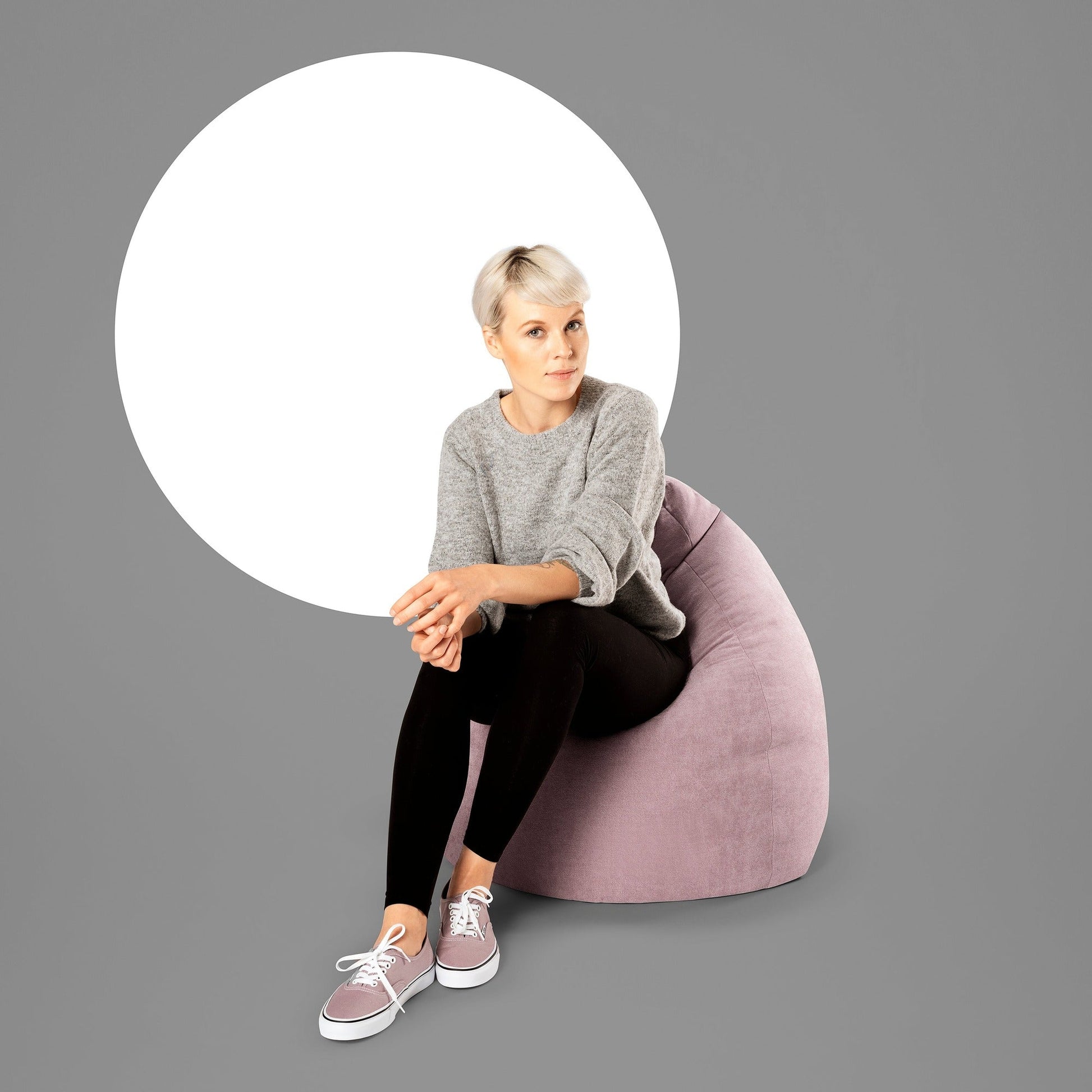 Woman sitting on a pink bean bag chair with a gray background
