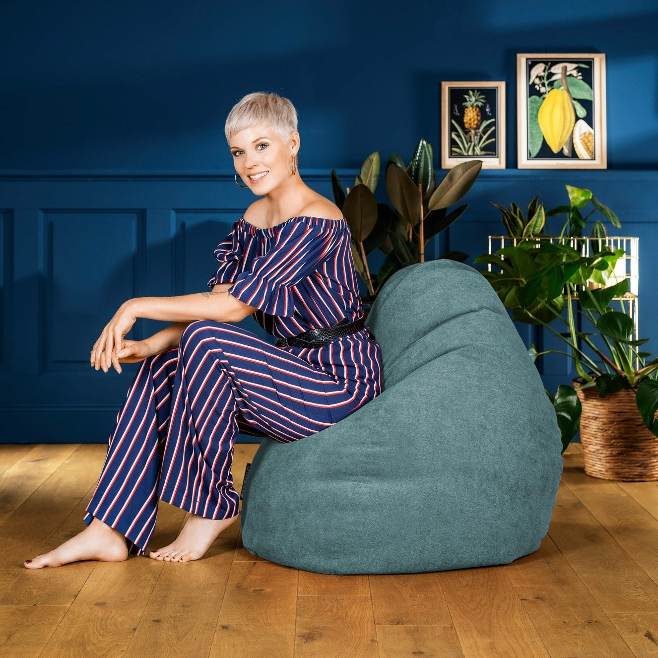 Woman sitting on a blue bean bag chair against a blue wall with framed pictures.