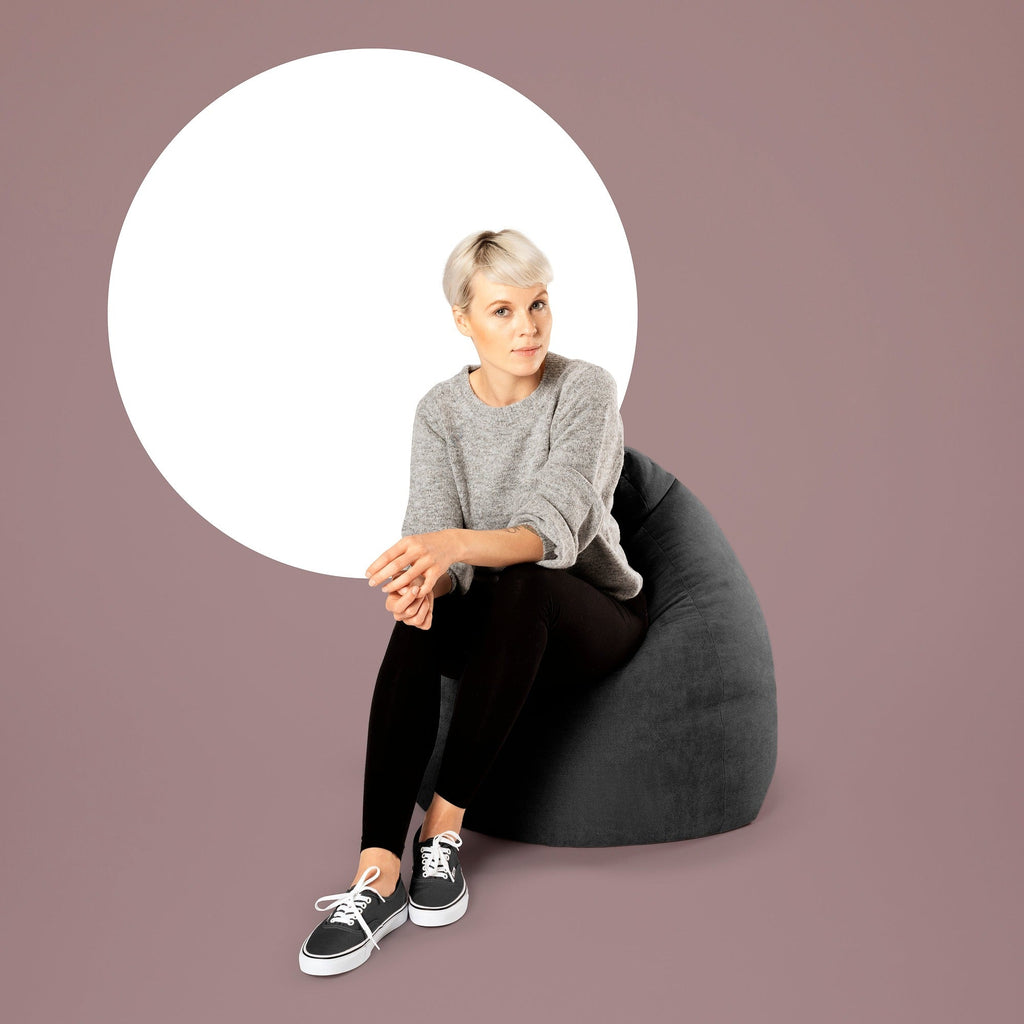 Woman sitting on a black bean bag chair against a purple background