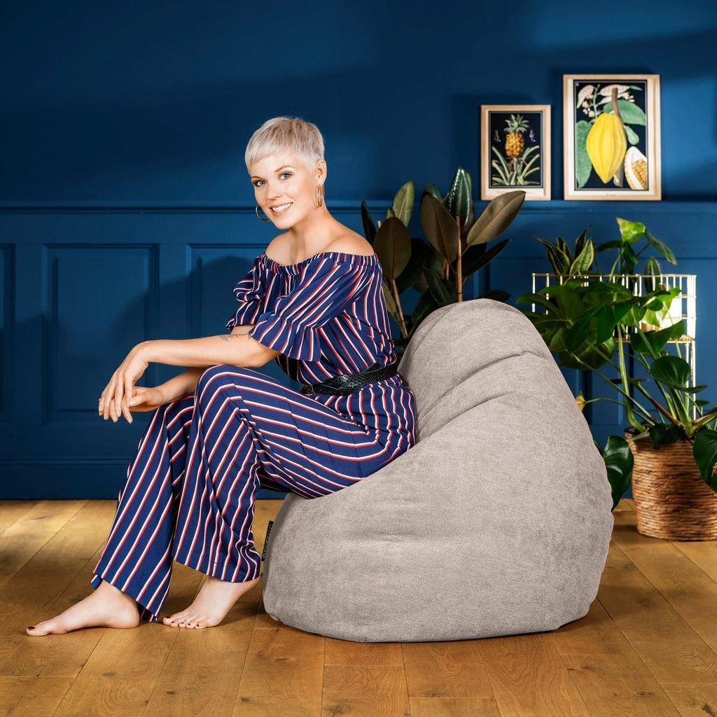 Woman sitting on a gray bean bag chair against a blue wall with decorative elements.