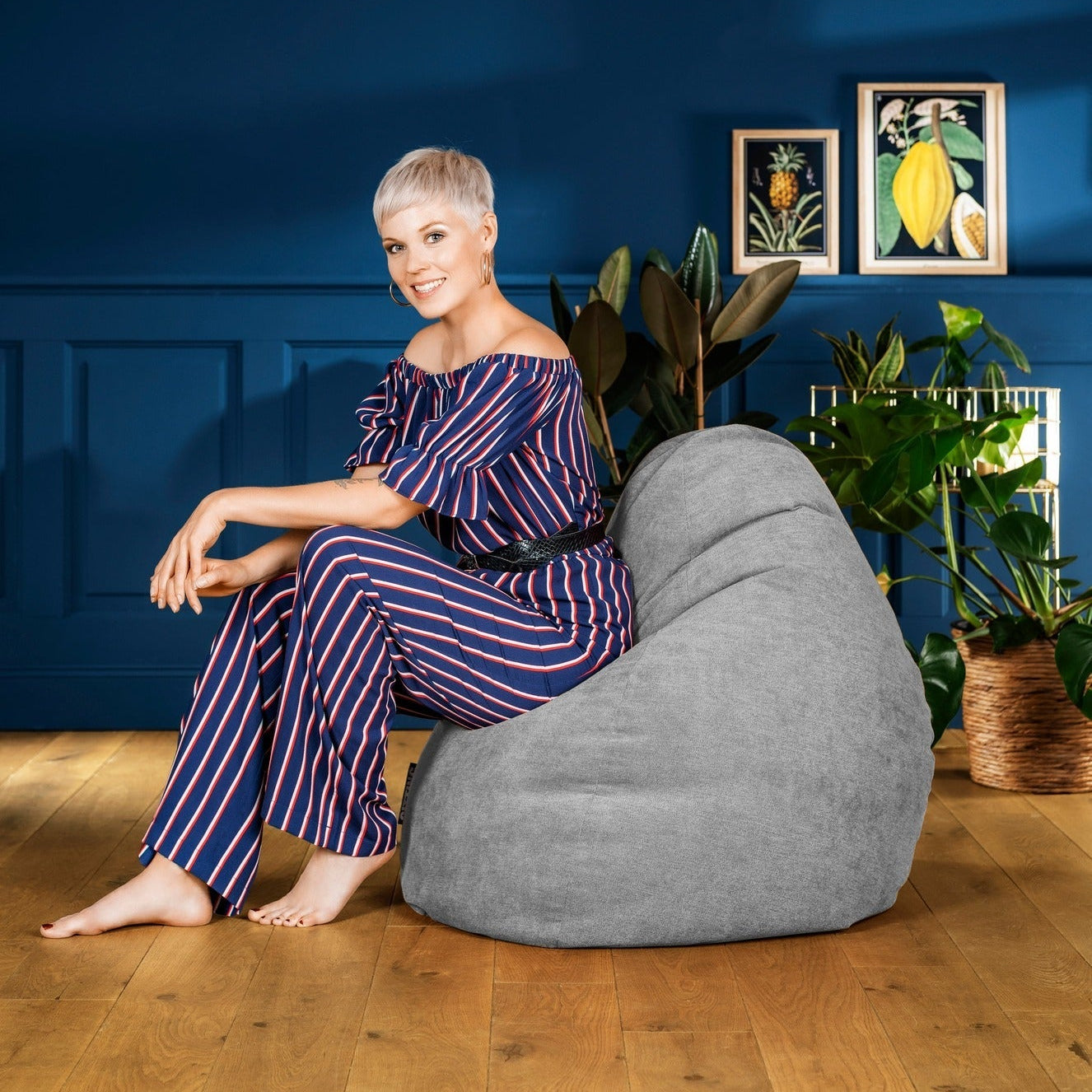 Woman sitting on a gray bean bag chair against a blue wall with decorative elements.