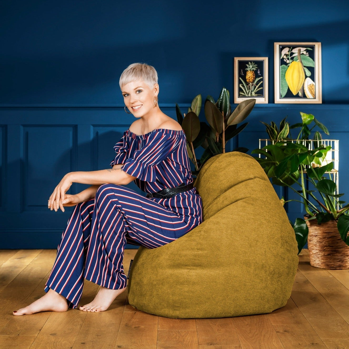 Woman sitting on a green bean bag chair against a blue wall with framed pictures.