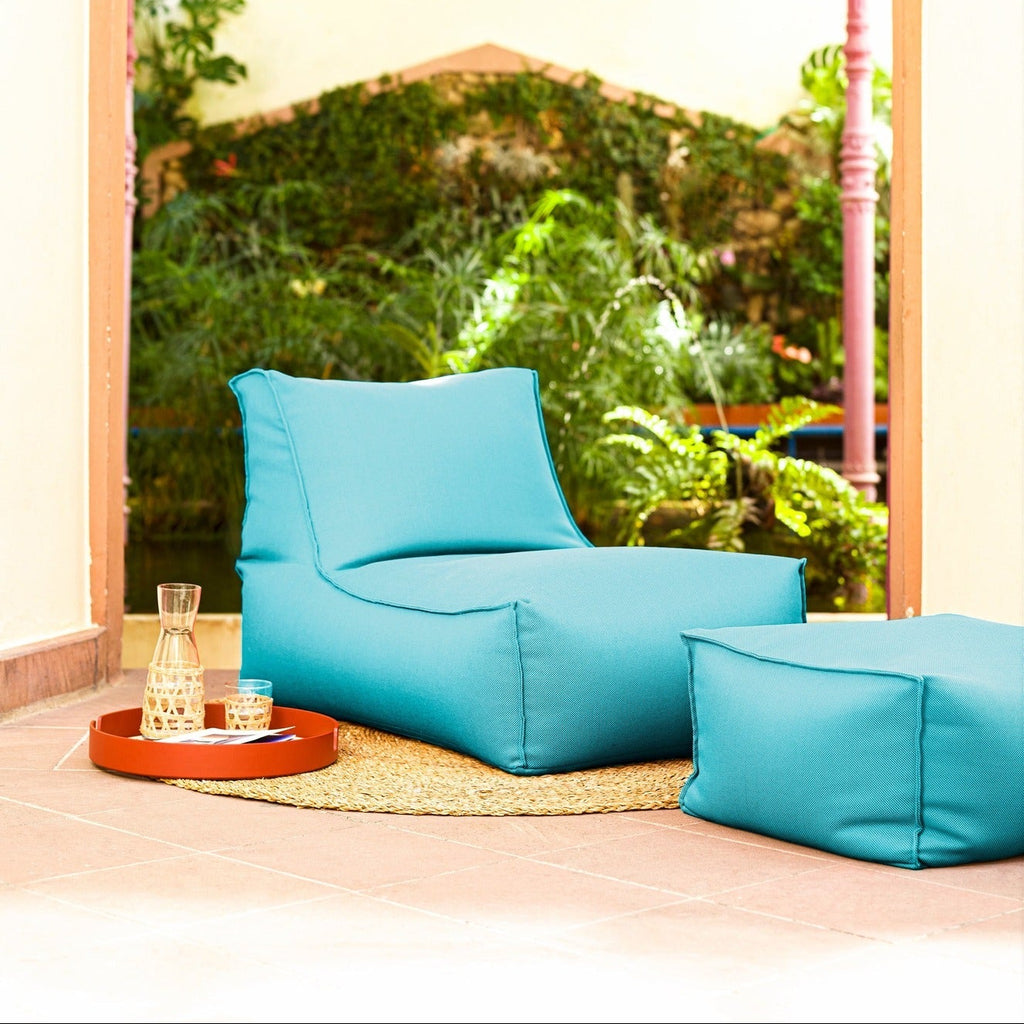 Turquoise bean bag chair and ottoman in a room with a large window view of greenery.