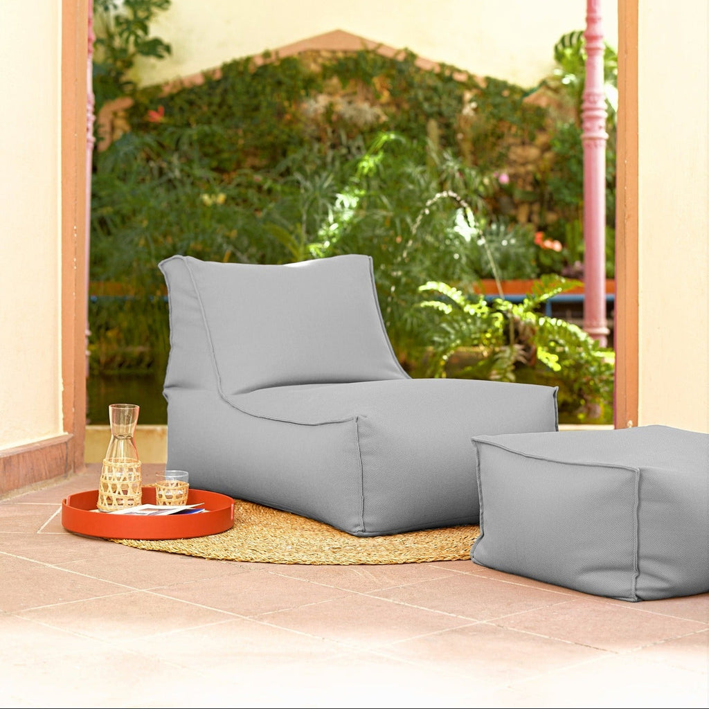 Gray bean bag chair and ottoman on a wooden floor with a garden view through an archway.
