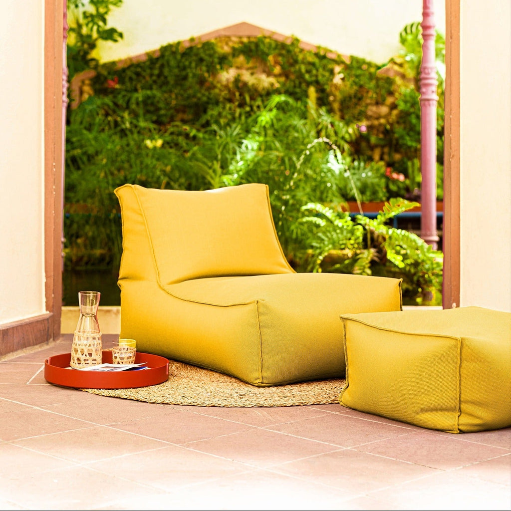 Yellow lounge chair and ottoman in a room with a large window view of greenery.