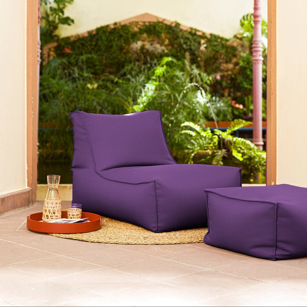 Purple bean bag chair and ottoman in a room with a large window view of greenery.