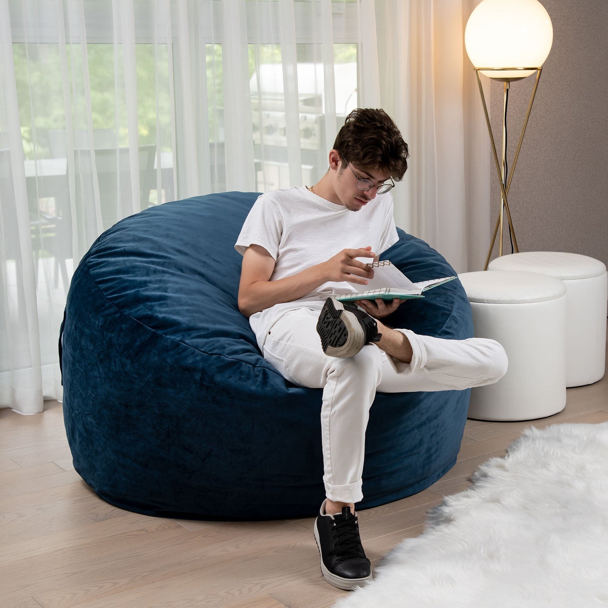 Person sitting on a large blue bean bag chair reading a book in a modern living room.