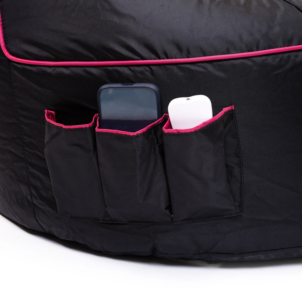 Black bean bag with pink trim featuring two pockets holding a phone and a white object on a white background.