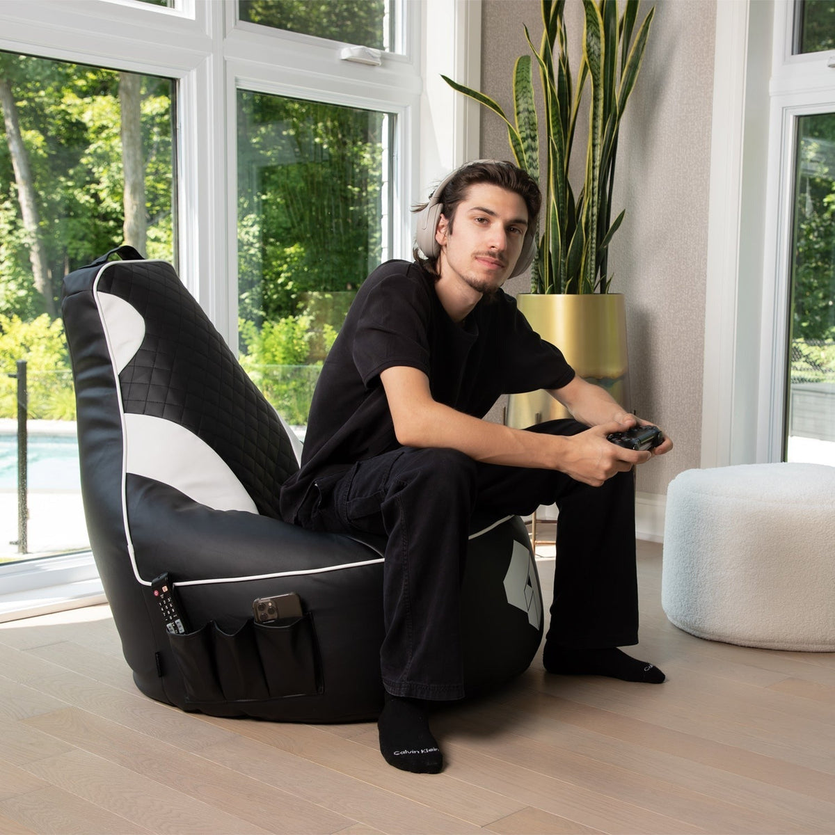 Person sitting on a black and white bean bag chair in a modern room with large windows.