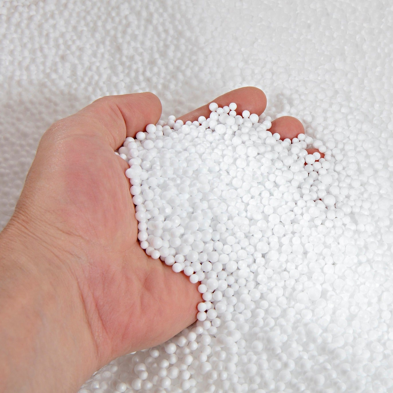 Hand holding white granules against a white background