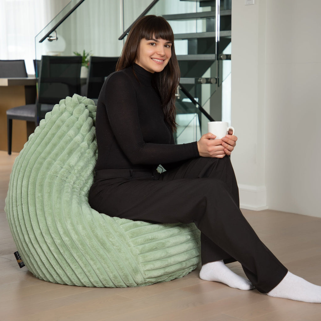 Woman sitting on a green bean bag chair holding a white mug in a modern indoor setting.