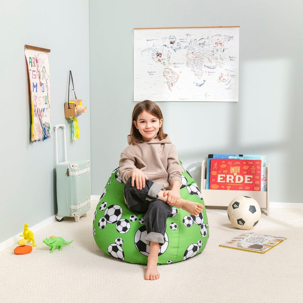 Child sitting on a green bean bag chair in a room with toys and books.