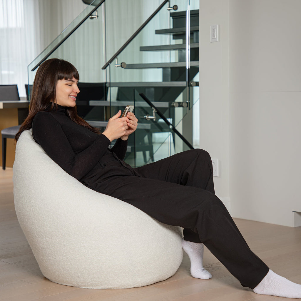 Woman sitting on a white bean bag chair using a smartphone in a modern interior setting.