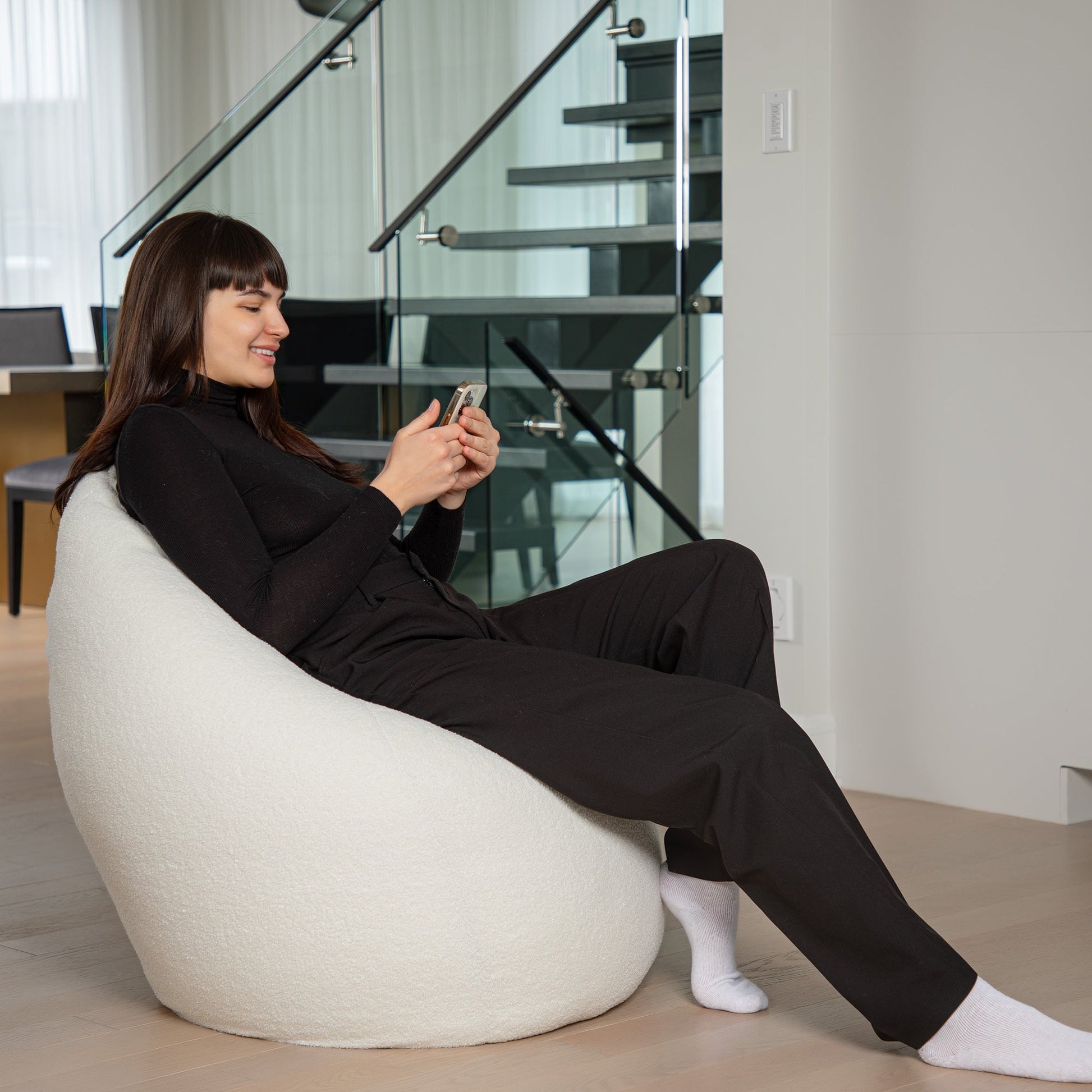 Woman sitting on a white bean bag chair using a smartphone in a modern interior setting.