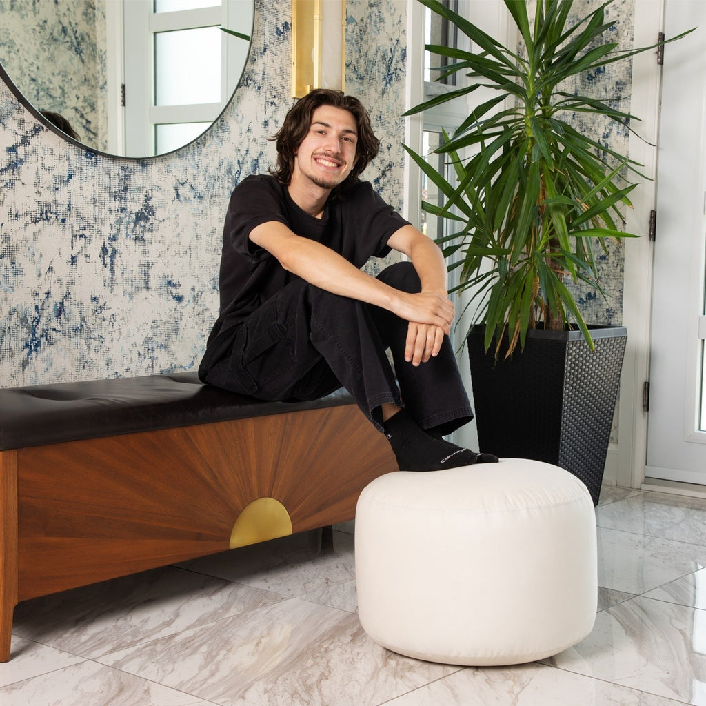 Man sitting on a bench in a stylish room with decorative wallpaper and a plant.