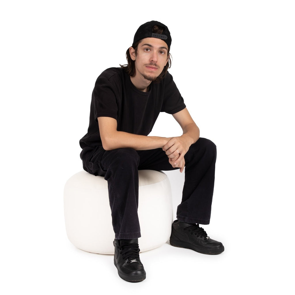Person wearing a black outfit sitting on a white chair against a white background