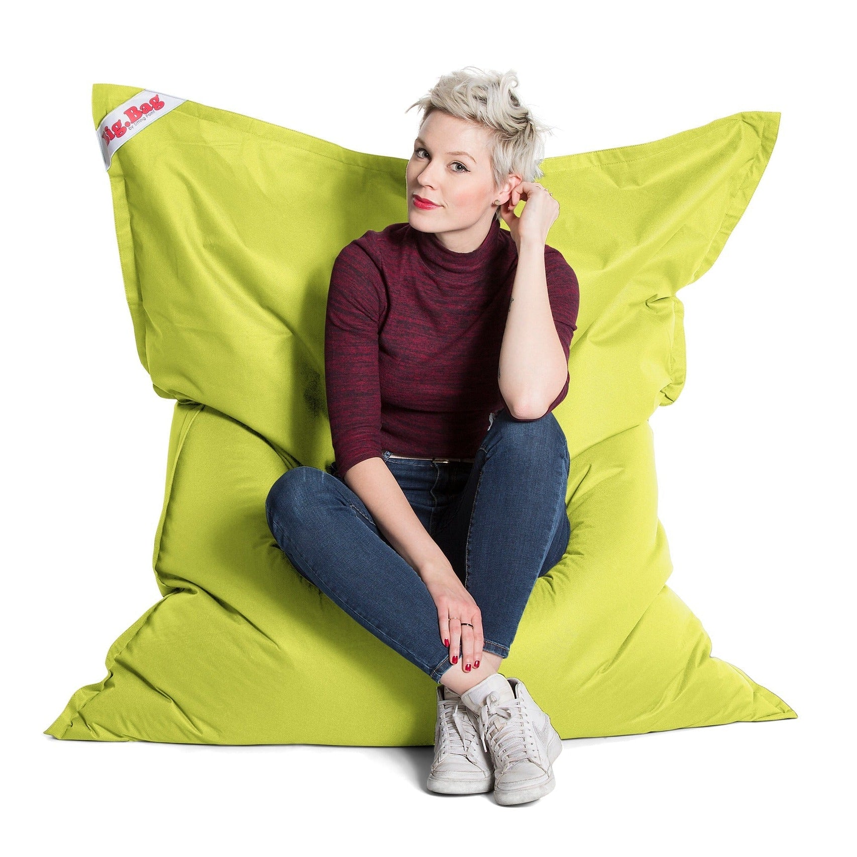 Woman sitting on a large green bean bag chair with a white background