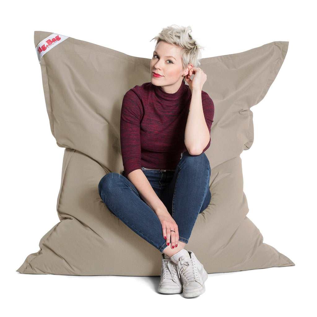 Woman sitting on a beige bean bag chair with a white background