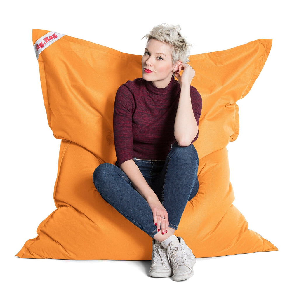 Person sitting on a large orange bean bag chair with a white background