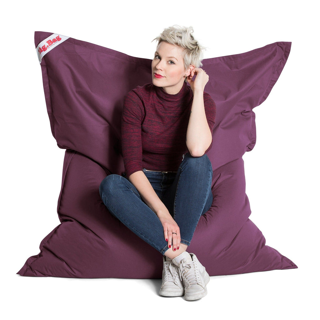 Woman sitting on a large purple bean bag chair with a white background