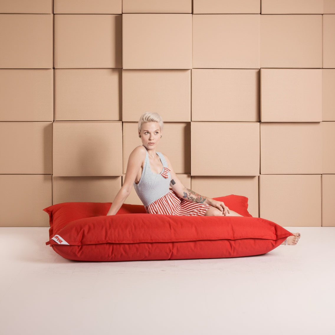 Woman sitting on a large red bean bag against a beige paneled wall.