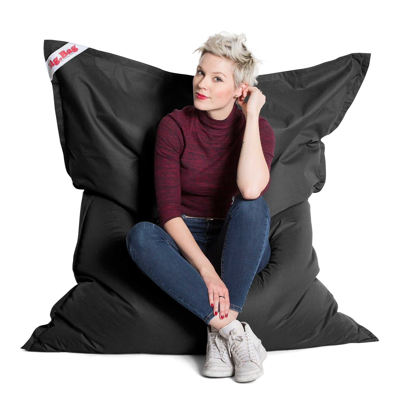 Woman sitting on a large black bean bag chair with a white background