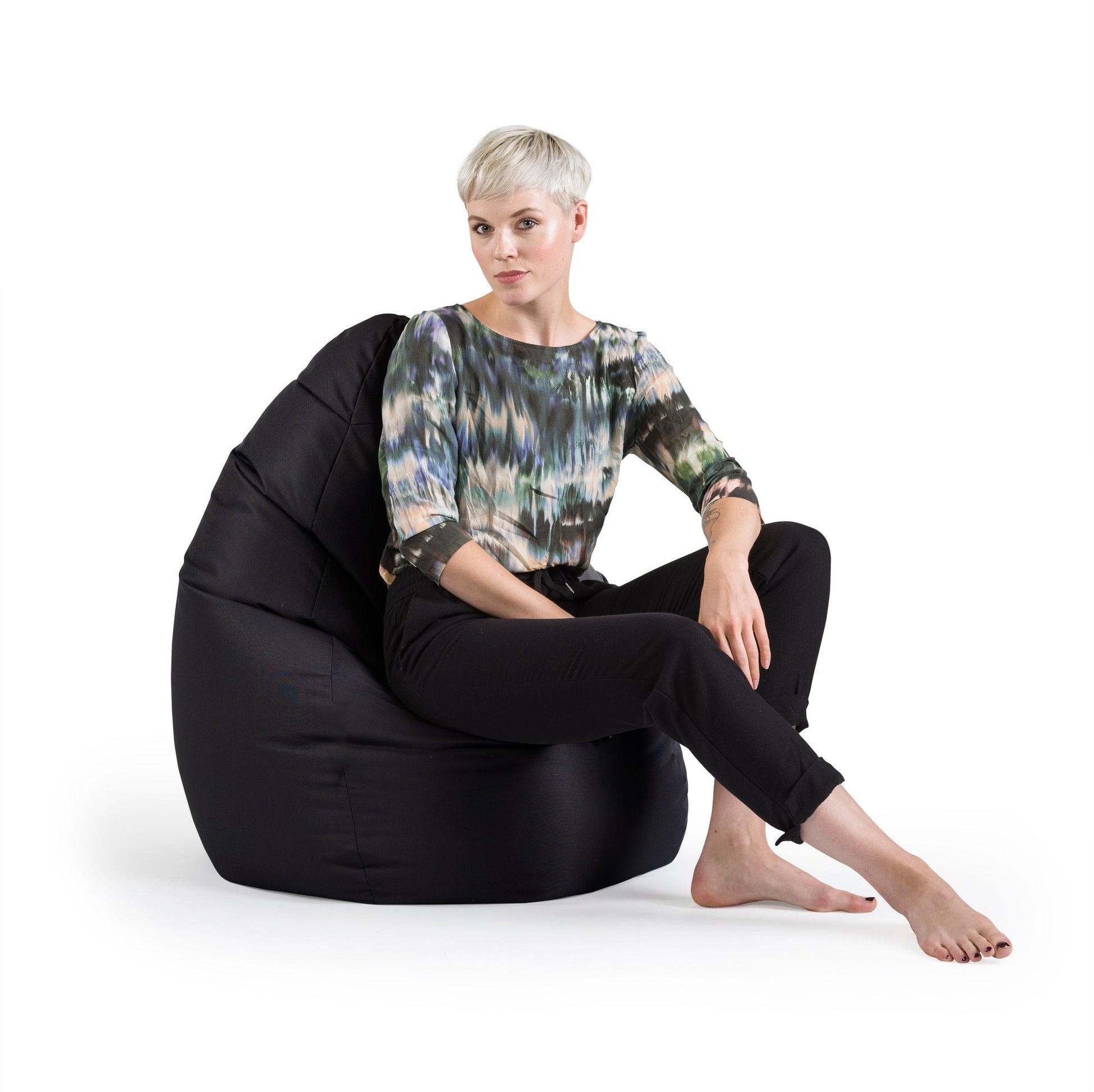 Woman sitting on a black bean bag chair against a white background