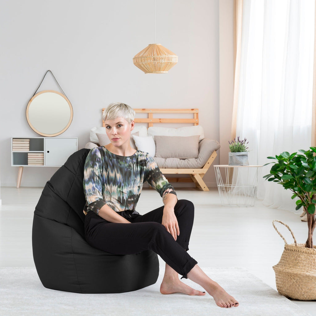 Woman sitting on a black bean bag chair in a modern living room.
