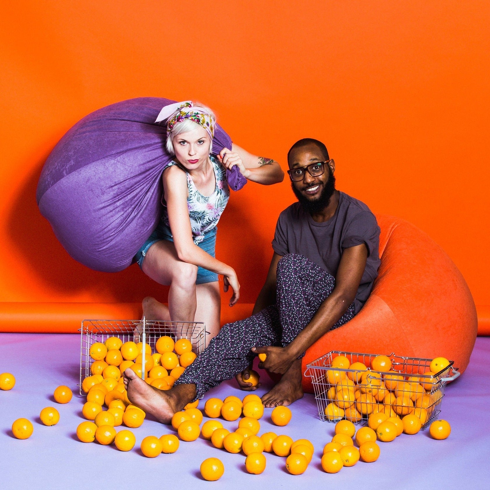 Two people surrounded by yellow balls on a purple floor with an orange wall background
