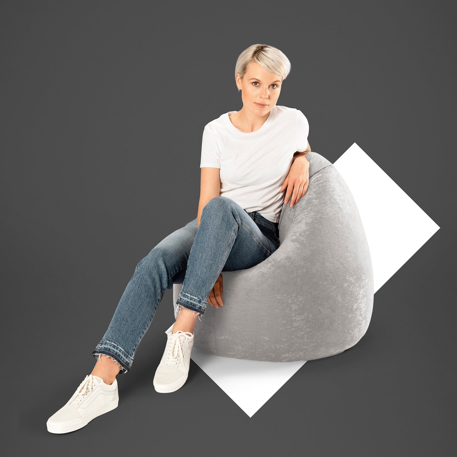 Woman sitting on a gray bean bag chair against a dark background