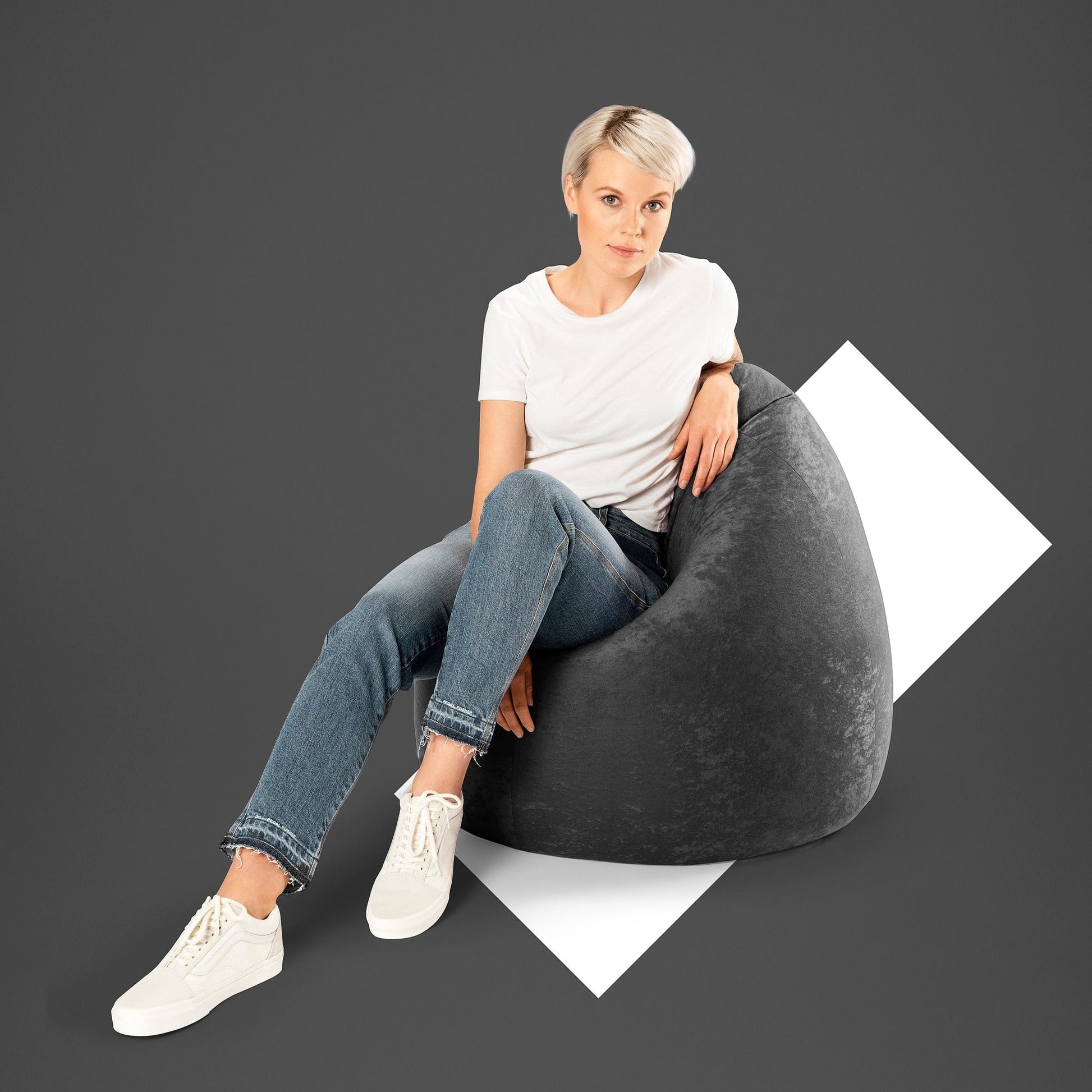 Woman sitting on a gray bean bag chair against a dark background