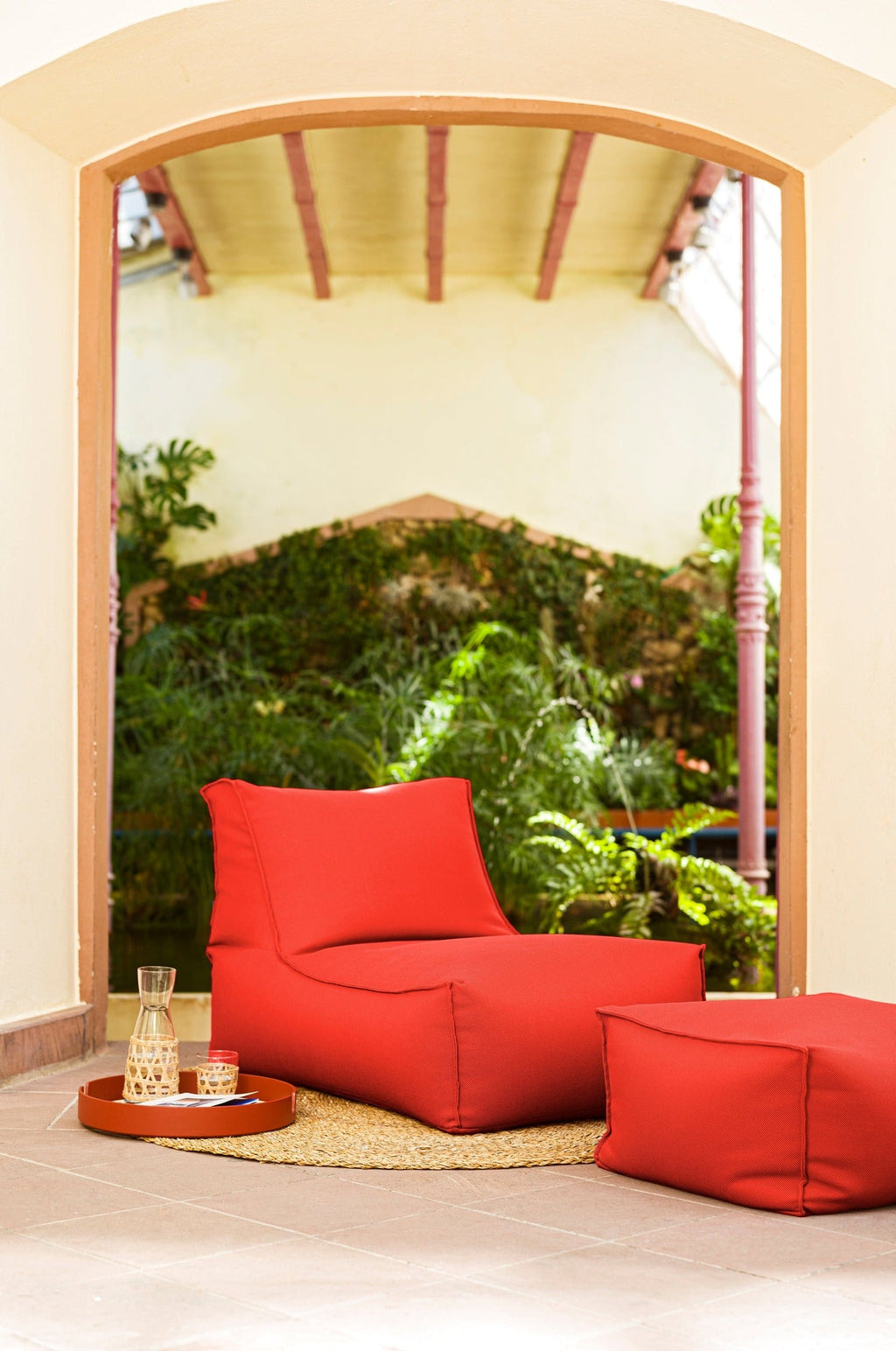Red bean bag chair and ottoman in a room with a large window showing greenery outside.