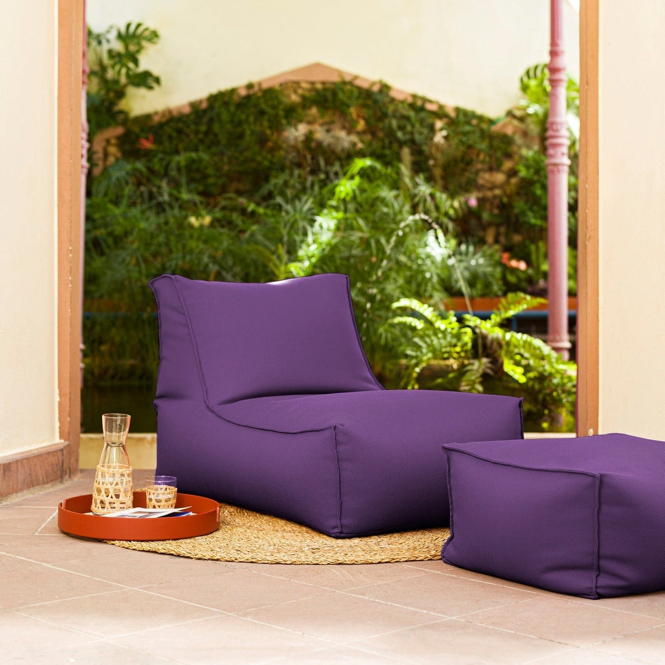 Purple bean bag chair and ottoman in a room with a large window view of greenery.