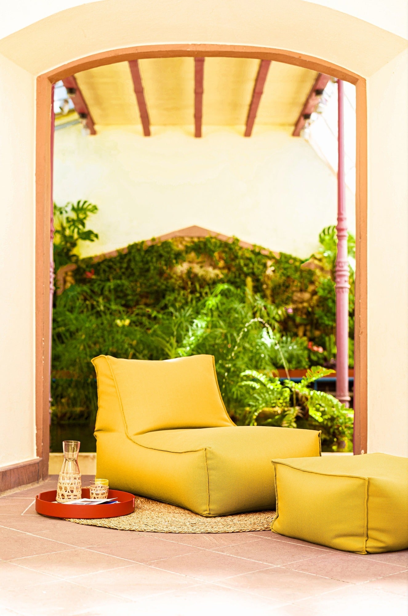 Yellow lounge chair and ottoman in a room with a large window view of greenery.