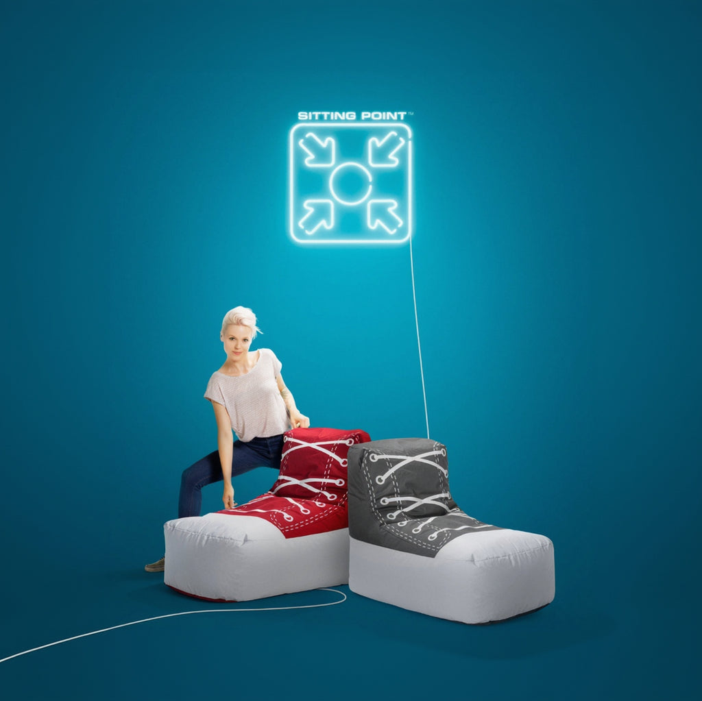 Person sitting on a large red and gray sneaker with a blue background and 'Sitting Point' logo.