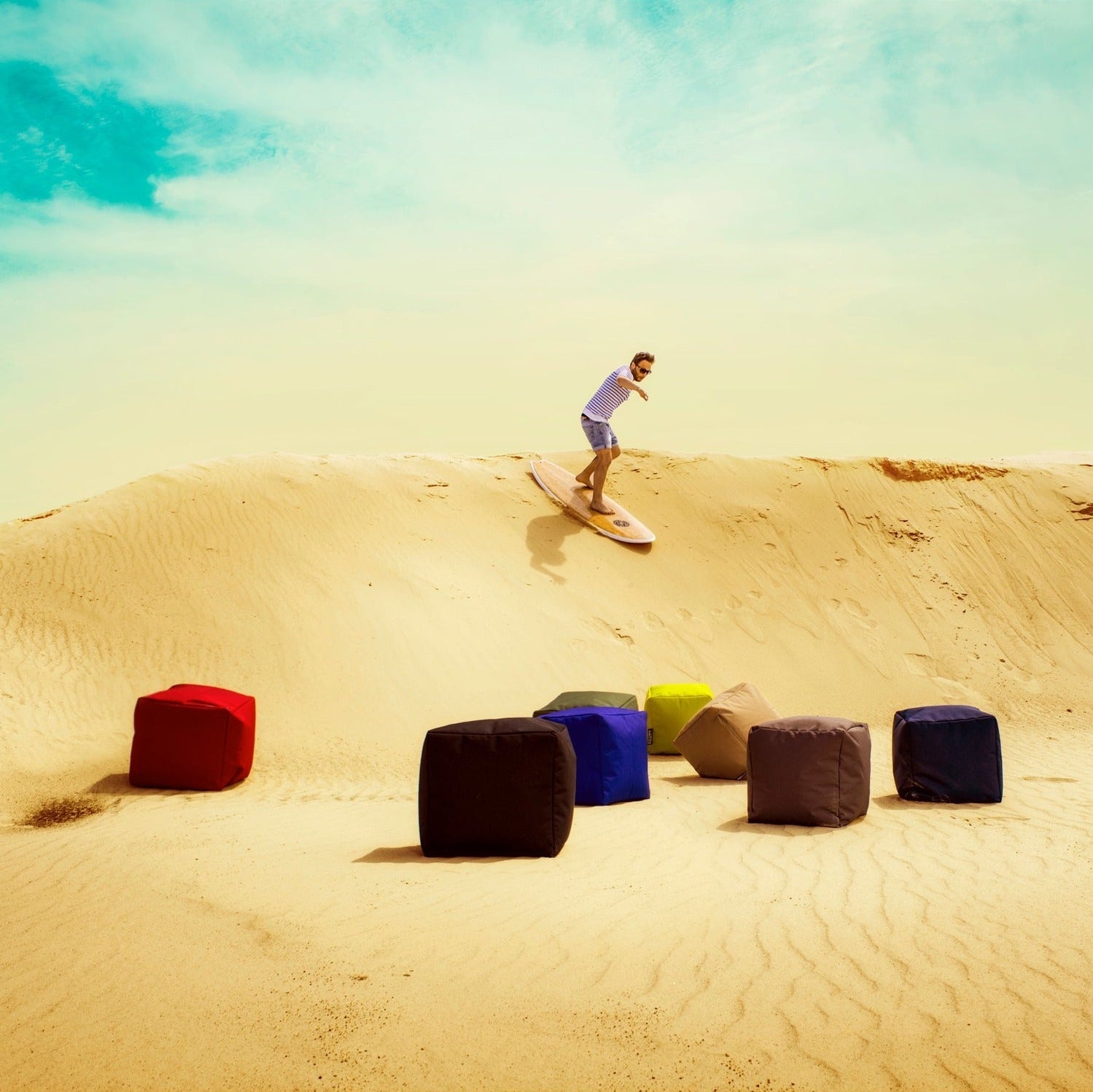 Person sandboarding down a dune with colorful bean bags in the foreground