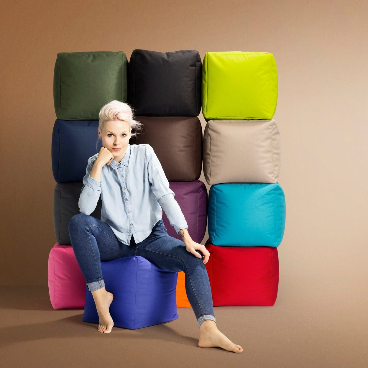 Woman sitting on a colorful stack of bean bags against a brown background