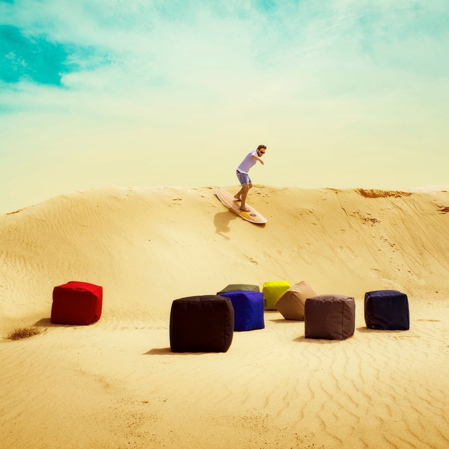 Person sandboarding down a dune with colorful cubes in the foreground