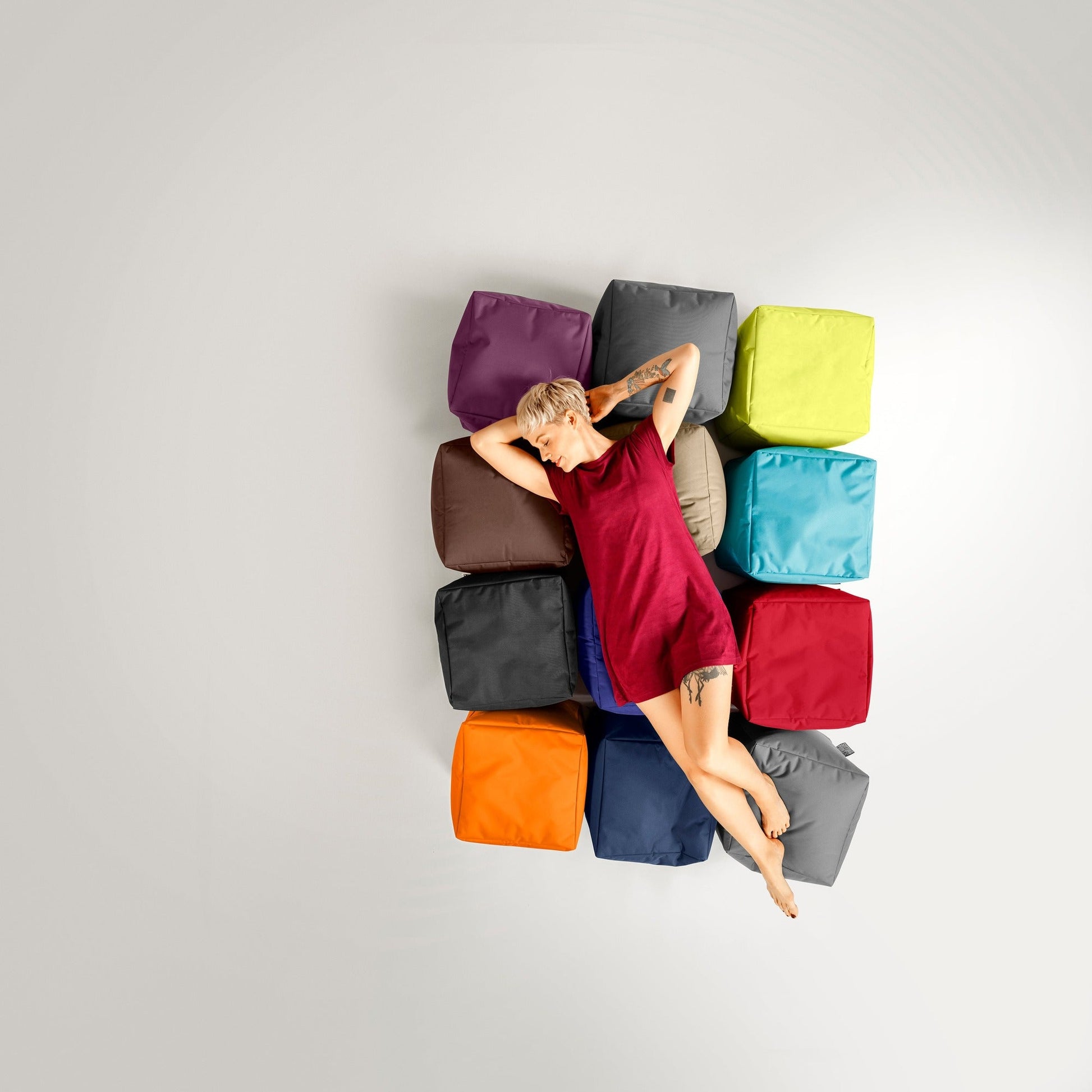 Person lying on a colorful arrangement of square cushions against a light gray background
