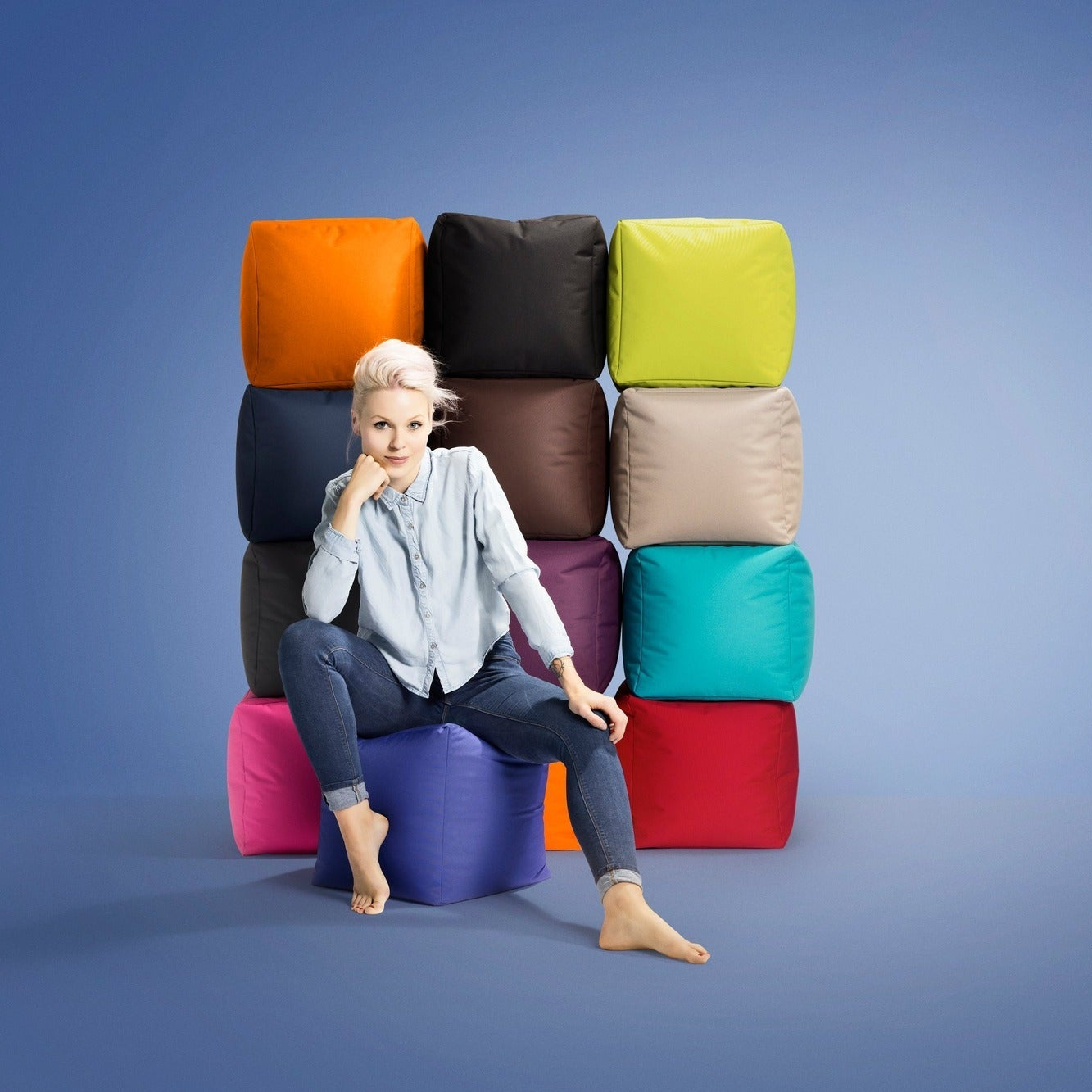 Woman sitting on a colorful stack of bean bags against a blue background