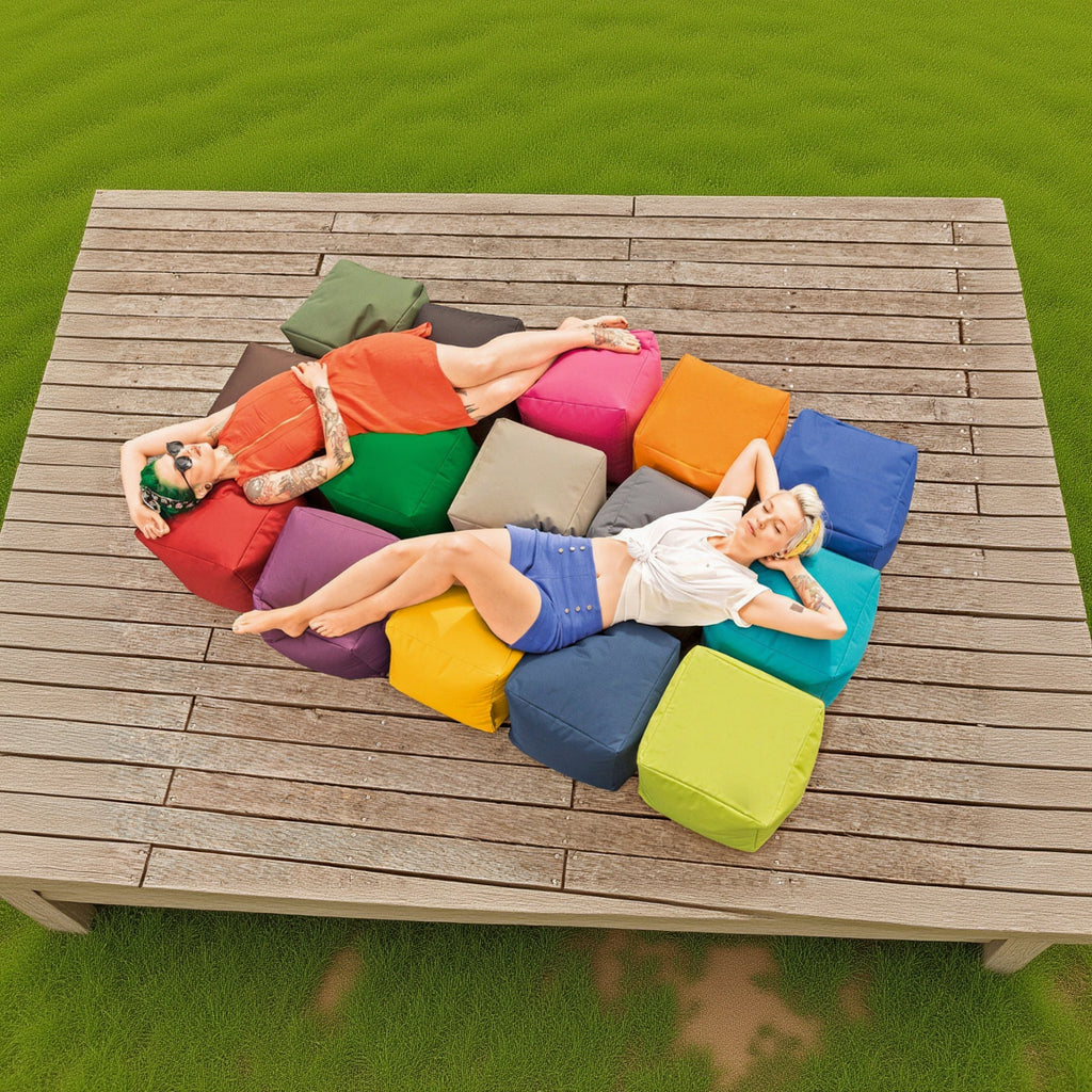 Two people lying on a wooden table with colorful cushions on a grassy background