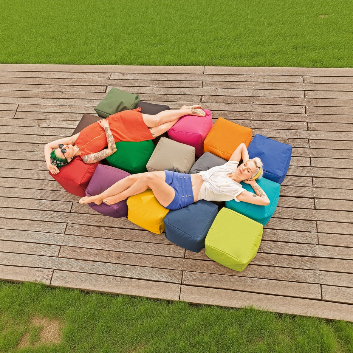 Two people lying on a colorful outdoor seating arrangement on a wooden deck.