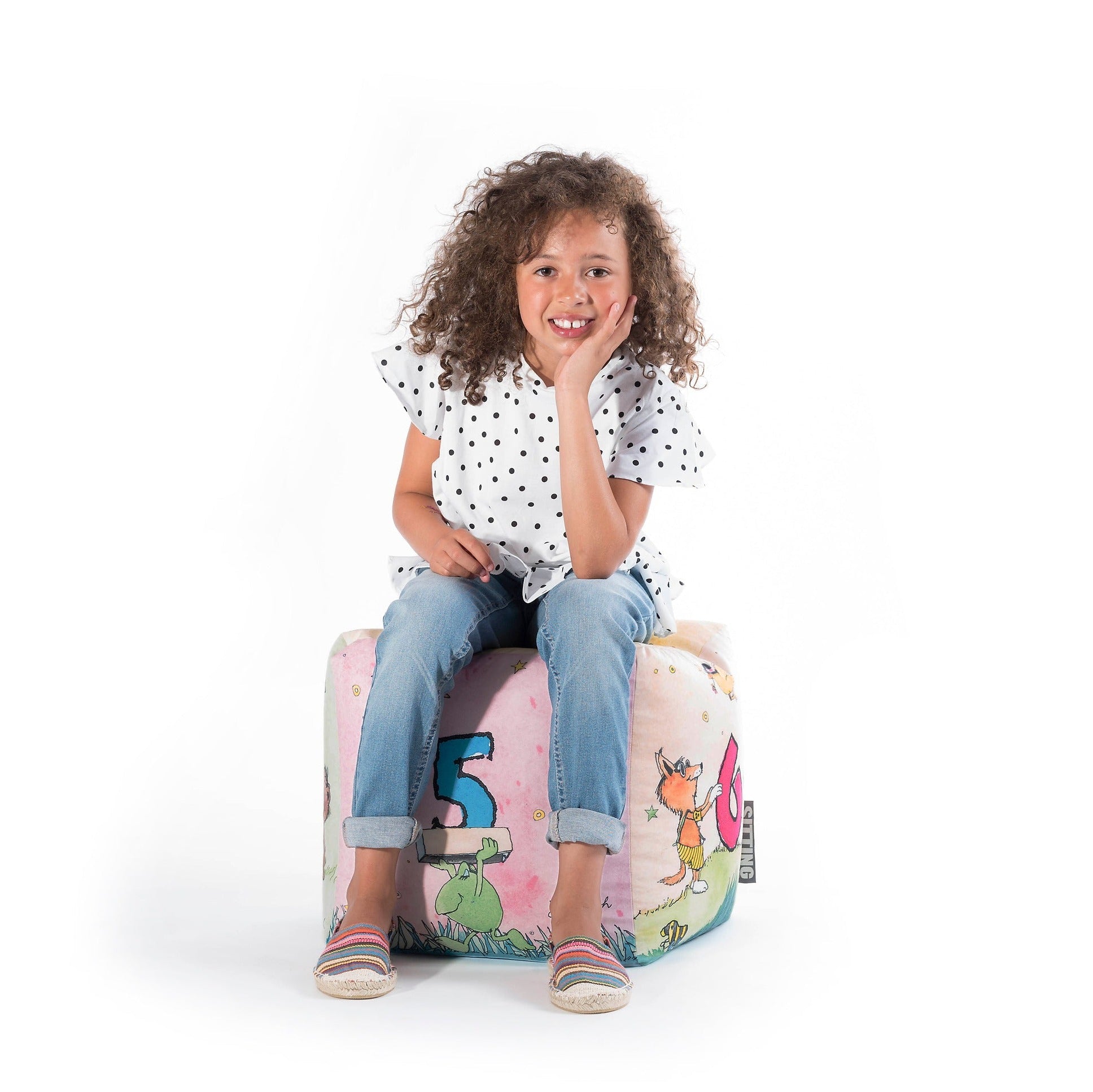 Child sitting on a colorful bean bag chair with cartoon characters on a white background