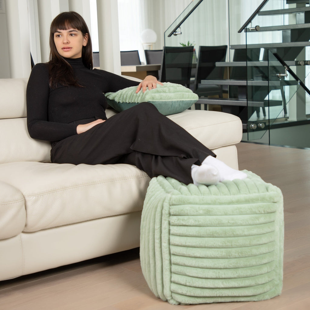 Woman sitting on a beige sofa with a green textured ottoman in a modern living room.