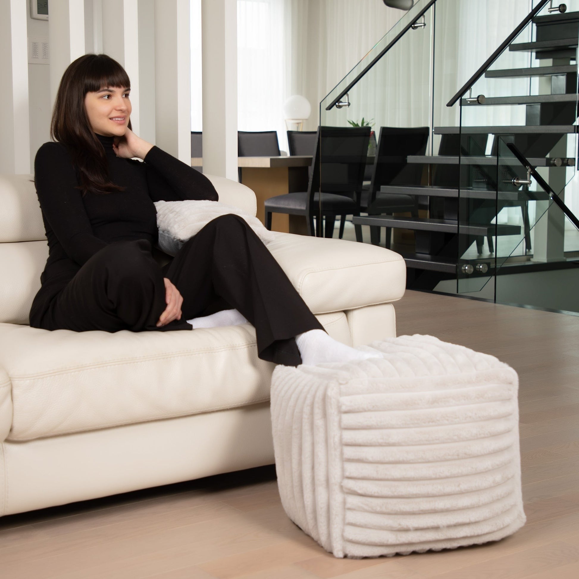 Woman sitting on a white sofa with a textured ottoman in a modern living room.